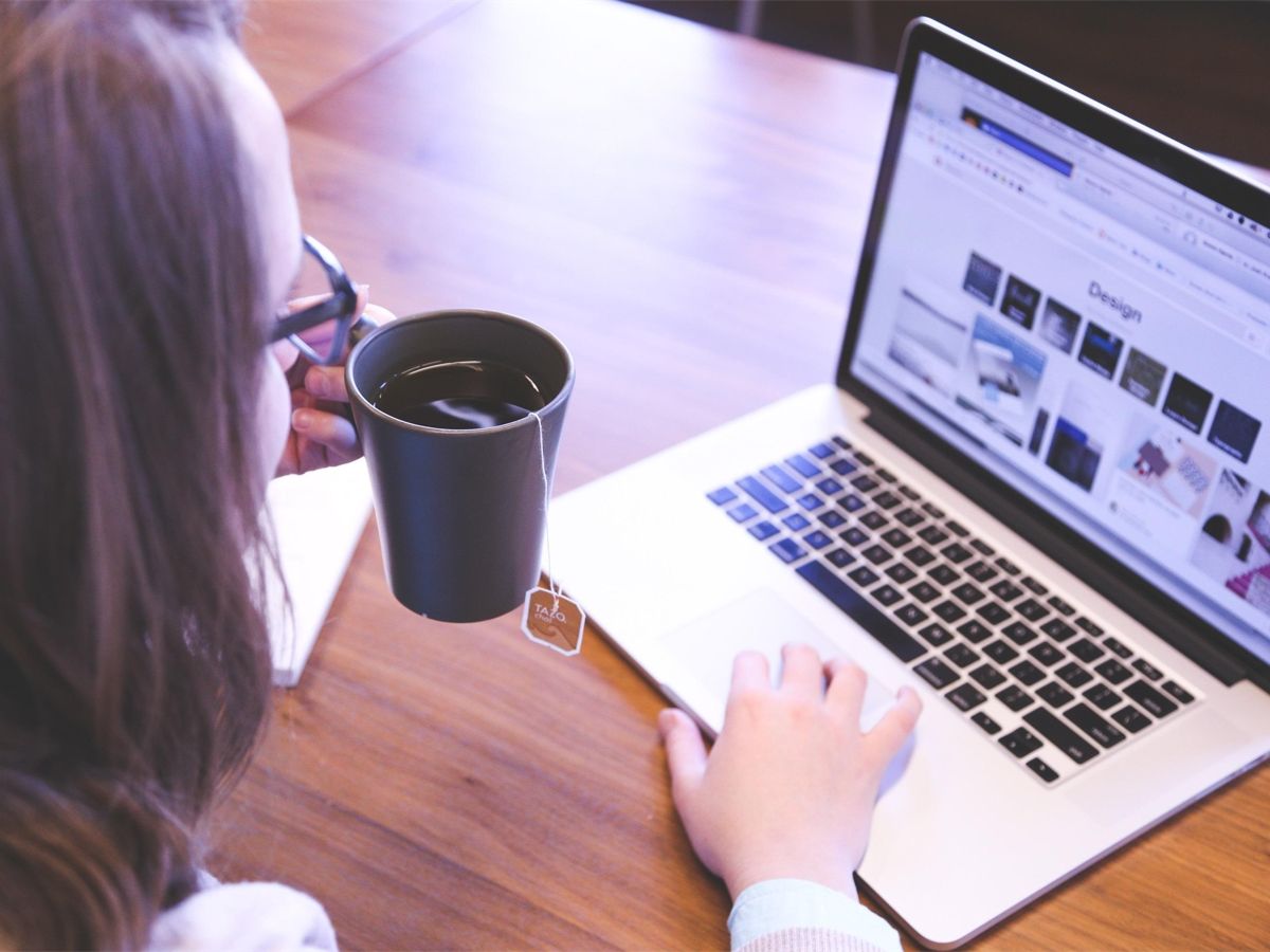 Over the shoulder image of a woman wearing glasses drinking tea, using her laptop - The most important metrics for content marketing - Image